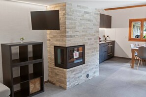 A modern living room with a stone fireplace, a flat-screen TV mounted above it, and a dining area with a table and chairs. - Charming apartment in an authentic village (Anniviers)