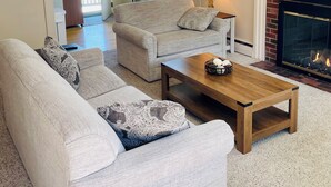 Ein Wohnzimmer mit einer Sofagarnitur, einem Couchtisch, einem Kamin und einem an der Wand befestigten Fernseher.