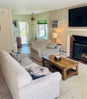 A living room with a sofa set, a coffee table, a fireplace, and a TV mounted on the wall. - Kennebunk Family Retreat Near Downtown with Beach Passes (Kennebunk)