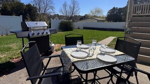 Eine Terrass mit Grill, Tisch für vier Personen und Stühlen.
