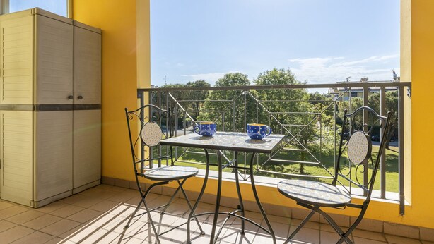 Ein Balkon mit Tisch und Stühlen, einem Kleiderschrank und Blick auf Grünflächen und Gebäude.