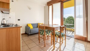 Eine Küche mit Herd, ein Esstisch mit Stühlen, eine Couch mit Kissen und ein Balkon mit Blick.