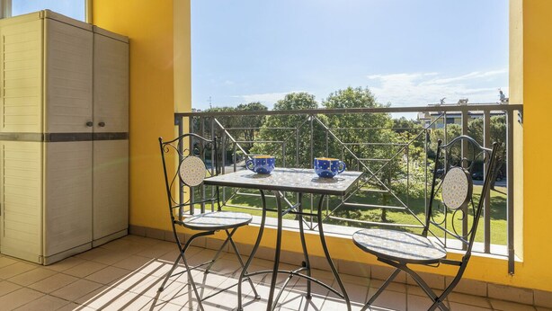 Ein Balkon mit Tisch und Stühlen, Blick ins Grüne und eine gelbe Wand.