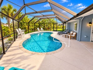 A swimming pool with a curved design, surrounded by lounge chairs and a covered patio area. - Punta Gorda Private Pool Vacation Home - Boat Ramp Access! (Punta Gorda)