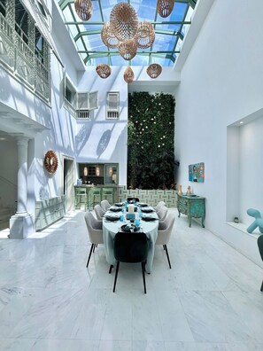 Un comedor moderno con techo de vidrio, pared verde con plantas y una mesa de comedor blanca para seis personas.