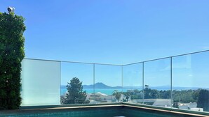 Una vista chiara di una piscina con un pontile in legno e una barriera in vetro, che si affaccia su un paesaggio panoramico con montagne e edifici.