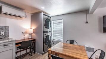 A compact kitchen with a wooden table, chairs, a built-in washing machine, and a wall-mounted TV.