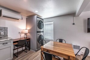 A compact kitchen with a dining area, built-in washer and dryer, and a flat-screen TV mounted on the wall. - Serenity Suites C (Corpus Christi)