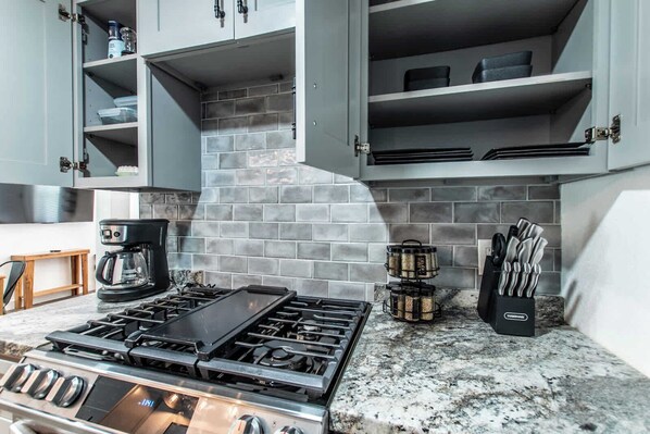 A kitchen with a gas stove, cabinets, a coffee maker, and a spice rack. - Serenity Suites C (Corpus Christi)