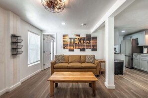 A modern living room with a sofa, coffee table, and artwork on the wall. - Serenity Suites C (Corpus Christi)