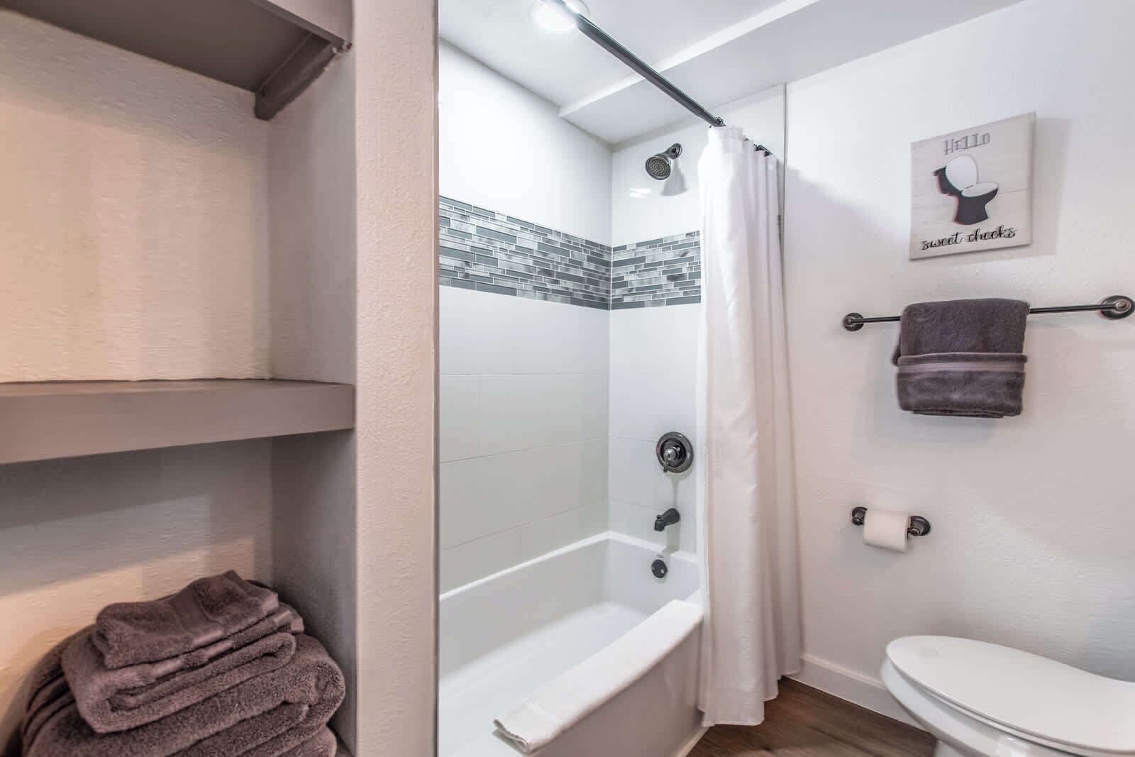 A bathroom with a shower, toilet, and a towel rack with towels.
