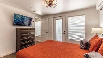 A bedroom with a large bed, a TV mounted on the wall, a ceiling light fixture, and a door leading to an outdoor area.