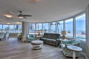 A spacious living room with a curved ceiling, large windows offering a view of the beach, a ceiling fan, and a variety of seating options. - Blue Horizon 2/2 Oceanfront AMAZING views, Pool, Hot tub, 27SE (Daytona Beach)