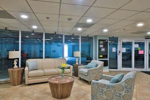 A lobby with a beige sofa, patterned armchairs, and a round wooden coffee table with a vase of flowers. - Whispering Waves: Luxury Oceanfront 2BR Condo; POOL, HOT TUB, GAME ROOMS, GYM (Daytona Beach)