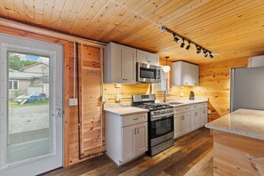 A kitchen with wooden walls, a stove, oven, microwave, and cabinets.