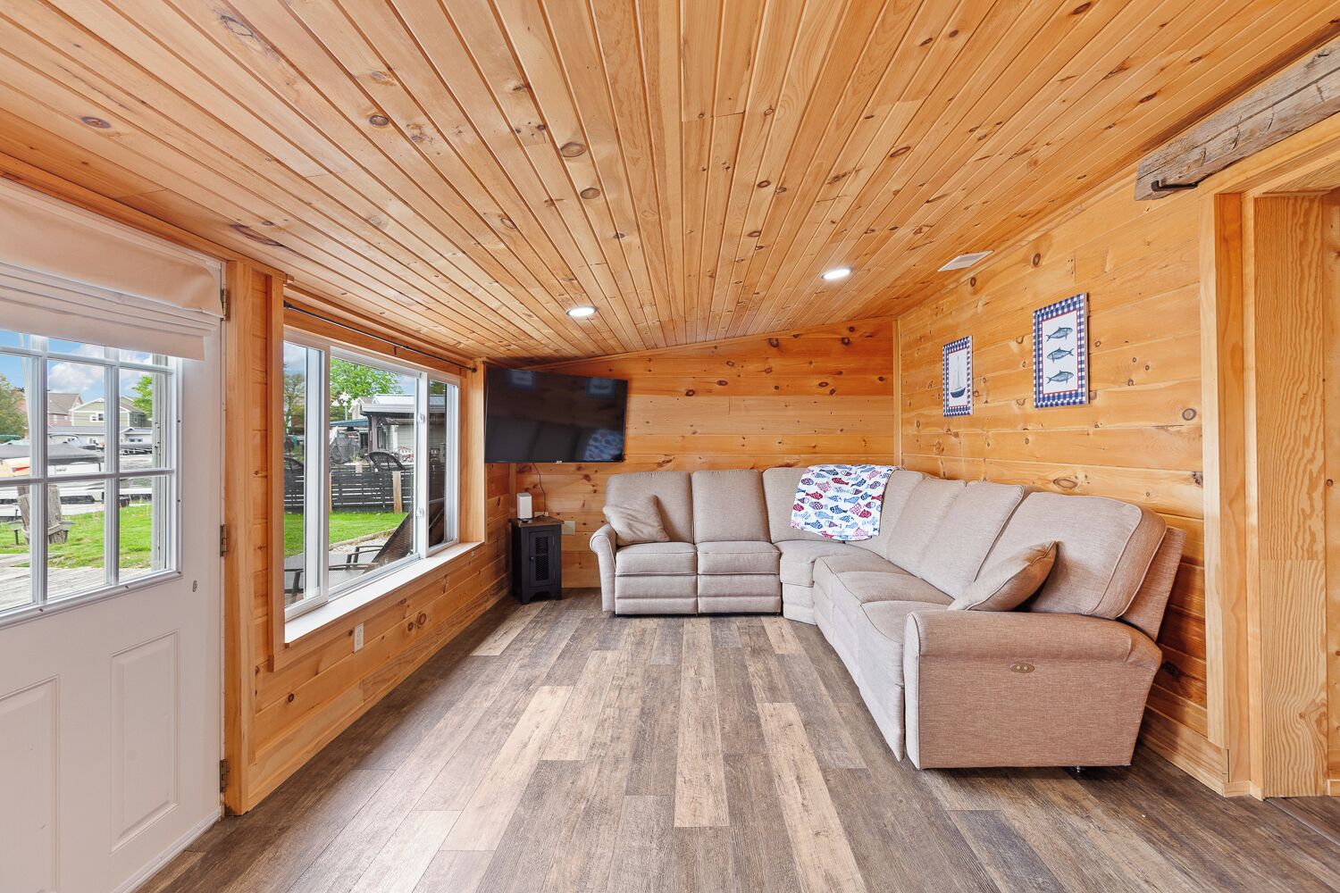 A wooden interior with a sectional sofa, a flat-screen TV, and a large window.