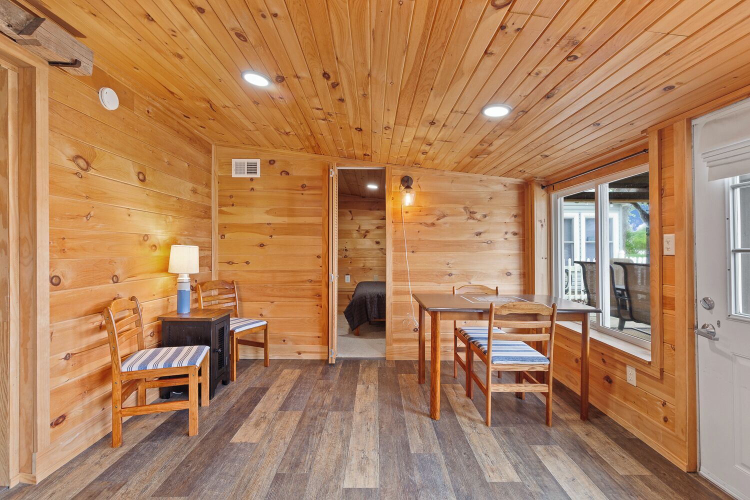 A wooden cabin interior with a dining area, a bed, and a window.