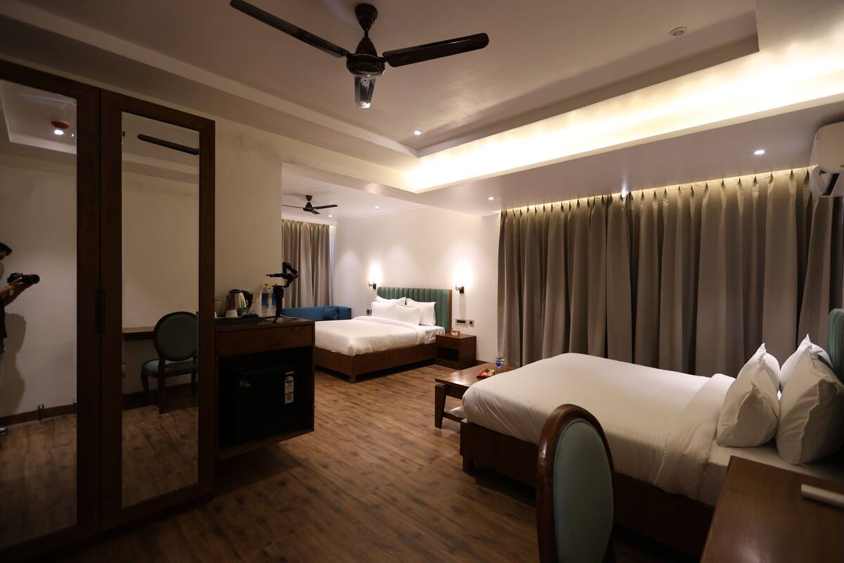 A hotel room with two beds, a desk, a chair, a mirror, a ceiling fan, and a window with curtains.