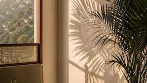 Un balcón con vistas a una colina, una planta en maceta, una silla de mimbre y una mesa con un libro.