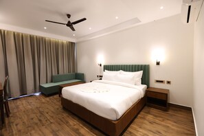 A modern hotel room with a large bed, a ceiling fan, a green sofa, and a nightstand. - Ventus Pines  (Kasauli)