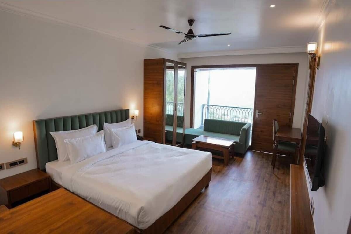 A hotel room with a bed, bedside tables, a ceiling fan, a balcony with a view, and a seating area.
