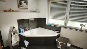 Un baño moderno con una bañera independiente, un tocador con espejo y una ventana con persianas.