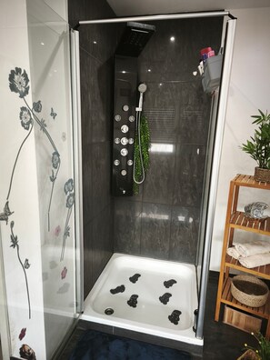 Een glazen douchecabine met een handdouche, een wit ligbad en een houten plank met handdoeken.