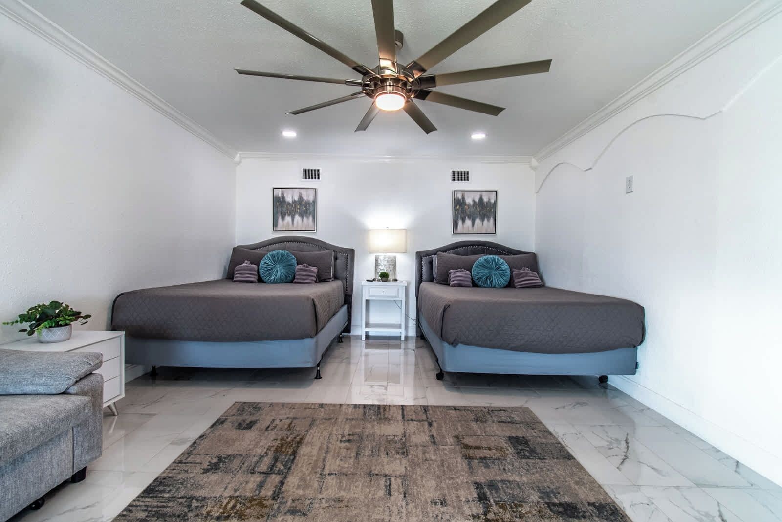 A bedroom with two beds, a ceiling fan, a nightstand, a lamp, and a rug.