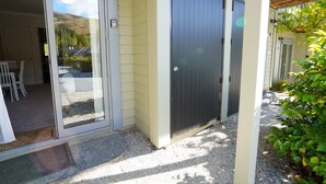 Un'area esterna riparata con una porta scorrevole in vetro che dà su un patio, una panca di legno e un vialetto sterrato.