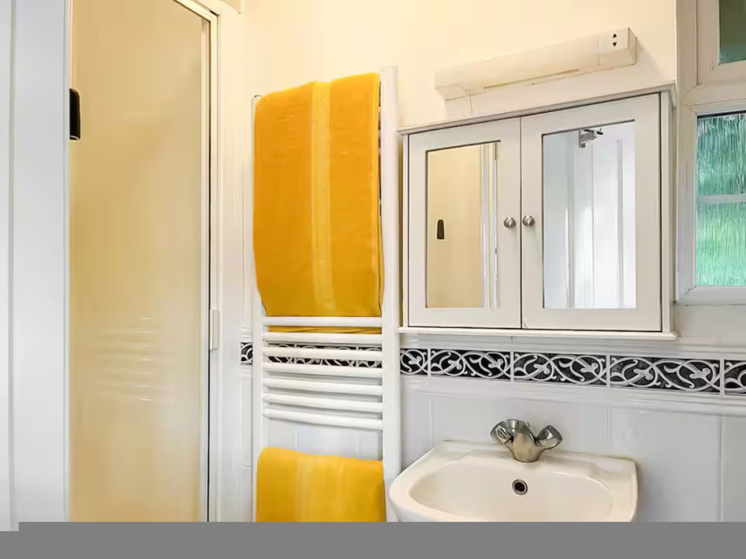 Une salle de bain avec un lavabo blanc, un miroir au-dessus et un porte-serviettes sur lequel est posée une serviette jaune.