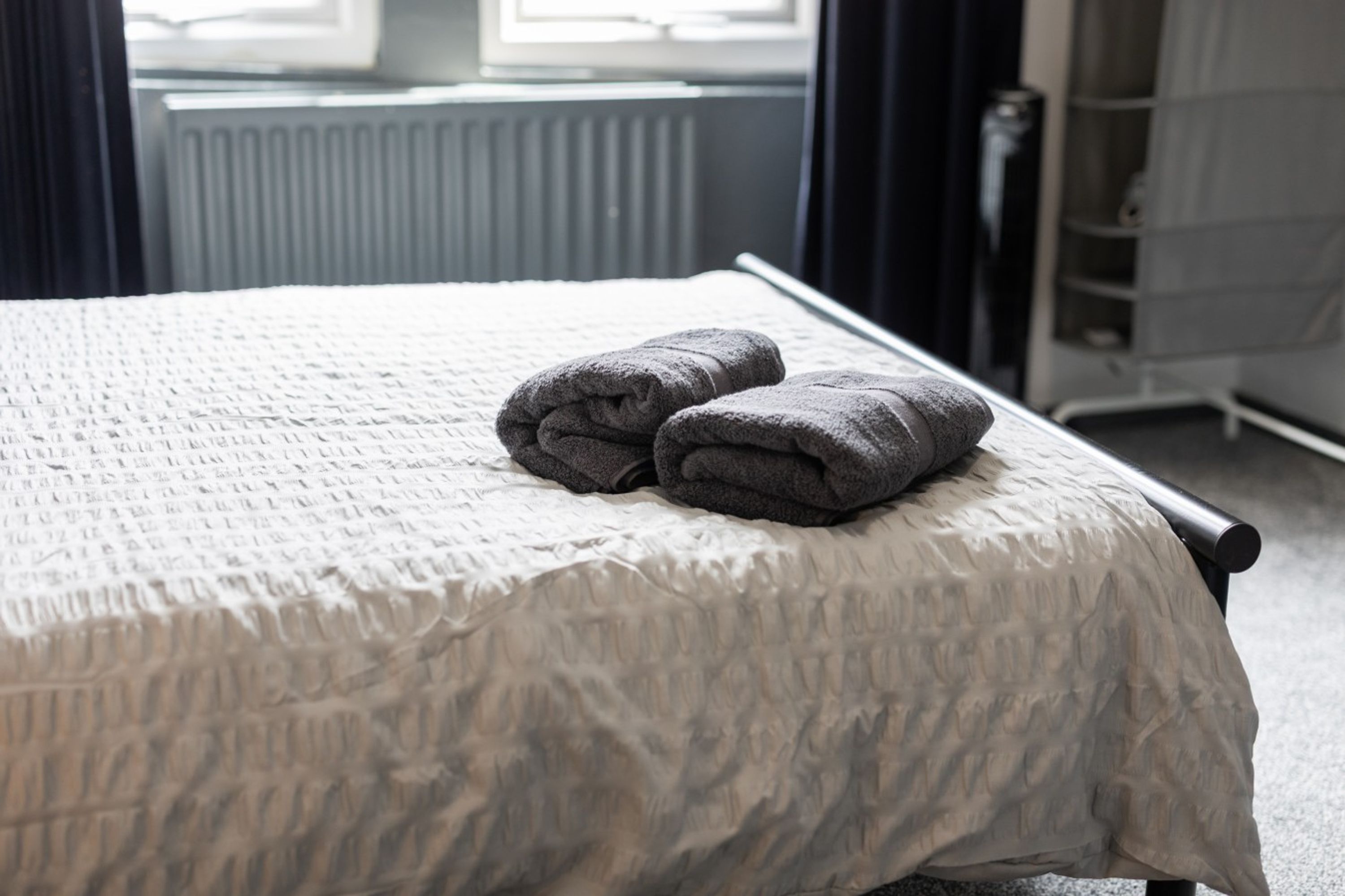 Een bed met een geribbeld wit laken en twee opgevouwen handdoeken erop.