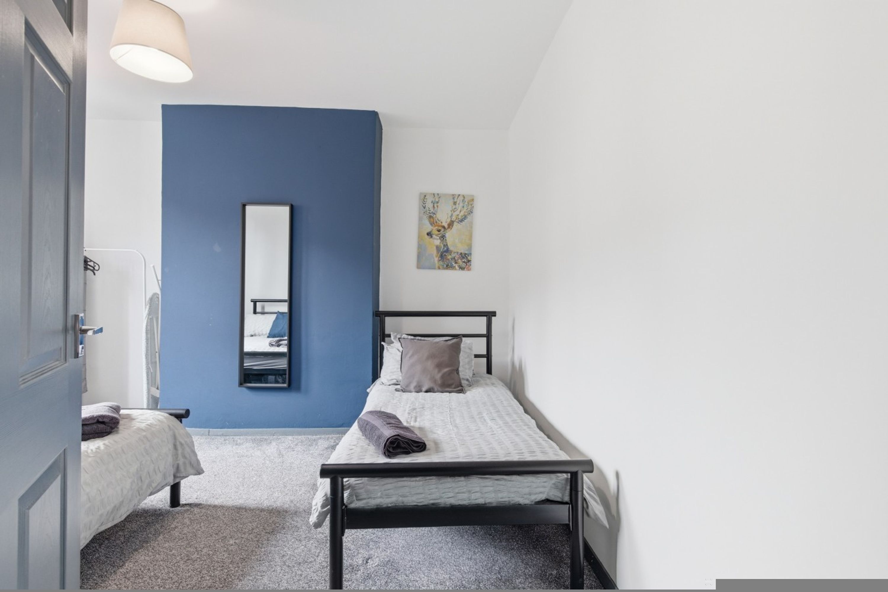 A bedroom with a single bed, a bedside table, a mirror, and a painting on the wall.
