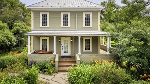 A two-story house with a porch, a front door, and a small front yard with flowers. - Heritage home with spa, EV charger and walkable village (Potton)