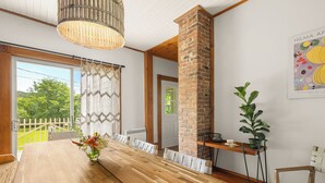 A dining area with a long wooden table, chairs, a brick column, a potted plant, and a wall-mounted artwork. - Heritage home with spa, EV charger and walkable village (Potton)