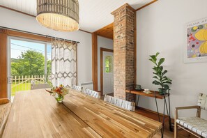 A dining area with a long wooden table, chairs, a brick column, a potted plant, and a wall-mounted artwork. - Heritage home with spa, EV charger and walkable village (Potton)