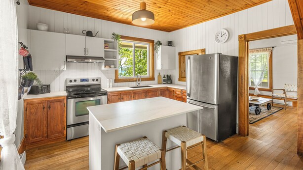 A kitchen with wooden cabinets, a stainless steel refrigerator, and a white island with stools. - Heritage home with spa, EV charger and walkable village (Potton)