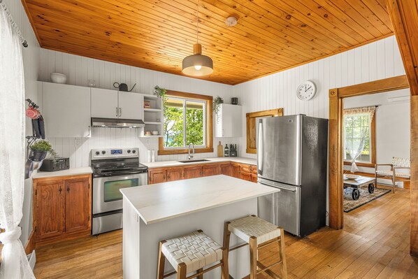 A kitchen with wooden cabinets, a stainless steel refrigerator, and a white island with stools. - Heritage home with spa, EV charger and walkable village (Potton)