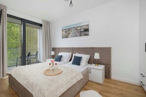 Un dormitorio moderno con una cama grande, una mesita de noche, una ventana con cortinas y un balcón con sillas.