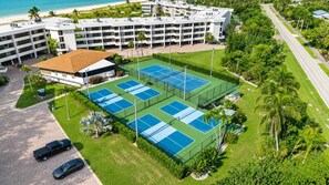 Vista aèria d'un hotel amb diverses pistes de tenis, una zona d'aparcament i una platja al fons.