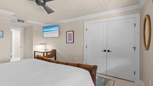 Ein Schlafzimmer mit einem großen Bett, einem Deckenventilator, einem Schreibtisch mit Stuhl, einem Fernseher und einem Kleiderschrank.