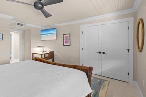 Ein Schlafzimmer mit einem großen Bett, einem Deckenventilator, einem Schreibtisch mit Stuhl, einem Fernseher und einem Kleiderschrank.
