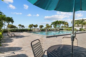 A pool area with a tiled deck, lounge chairs, and a table under a canopy. - Gulf Front Retreat at Gulfside Place (Sanibel)