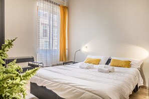 Ein Hotelzimmer mit Bett, Schreibtisch, Stuhl, Lampe und einem Fenster mit Vorhängen.