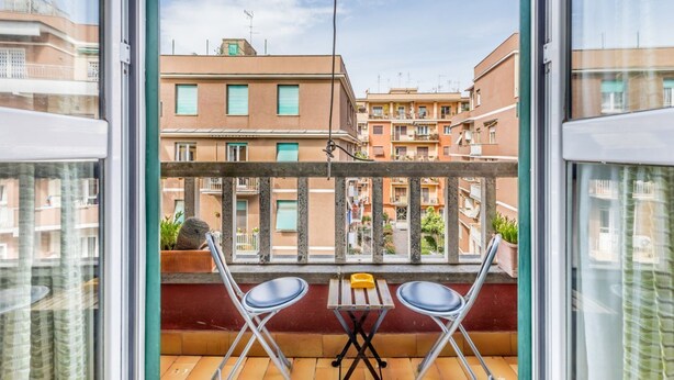 Un balcon avec deux chaises et une petite table, donnant sur une rangée d’immeubles d’habitation.
