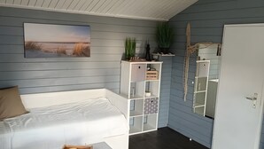 Quarto com cama branca, caixa organizadora, espelho e um letreiro de boas-vindas em uma prateleira.