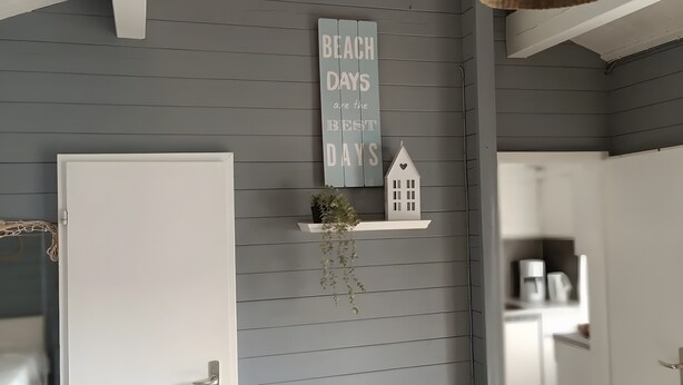 Um corredor com parede cinzenta, porta branca, uma placa que diz 'BEACH DAYS are the BEST DAYS', uma pequena decoração em formato de casa e uma planta pendente.