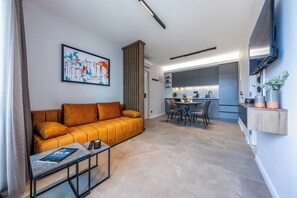 Ein modernes Wohnzimmer mit einer Couch, einem Couchtisch und Kunstwerken, das in einen Küchenbereich mit Esstisch und Stühlen übergeht.