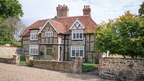 A stone house with a tiled roof, multiple windows, and a gravel driveway. - Challens Yarde is a large double fronted cottage, providing spacious, bright, and airy accommodation (Midhurst)