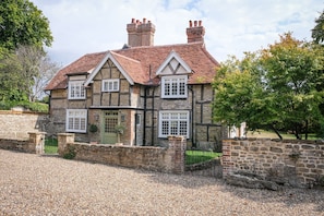 A stone house with a tiled roof, multiple windows, and a gravel driveway. - Challens Yarde is a large double fronted cottage, providing spacious, bright, and airy accommodation (Midhurst)