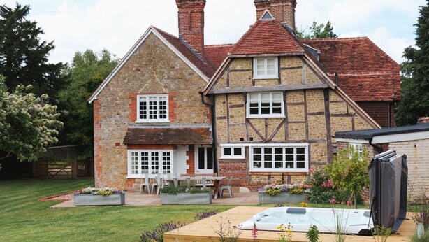 A stone house with a wooden deck, a hot tub, and a garden with flowers and plants. - Challens Yarde is a large double fronted cottage, providing spacious, bright, and airy accommodation (Midhurst)